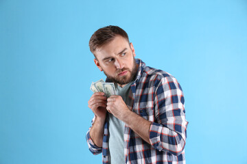 Greedy young man hiding money on light blue background