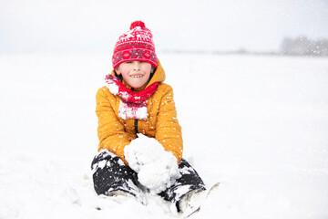 Fototapeta na wymiar Funny little boy in colorful clothes playing outdoors during a snowfall. Active holidays with children in winter on cold snowy days. Happy child is having fun and playing in winter.