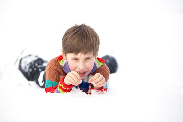 Fototapeta premium A funny little boy in colorful clothes lies in the snow. A hardened child in winter.