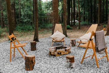 Wooden chairs around the fireplace. Pine forest. Family holidays in the country, fun trips in the fresh air. Rest on a picnic at a camping site.