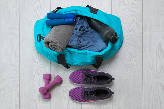 Bag with different sports equipment on wooden floor, flat lay