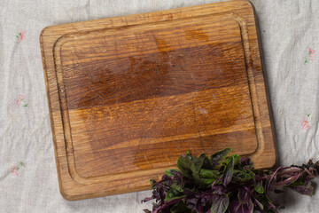 Cutting wood board and bunch of green basil on gray background