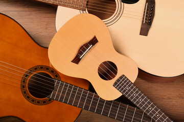 Ukulele and acoustic guitars on wooden background, flat lay. String musical instruments
