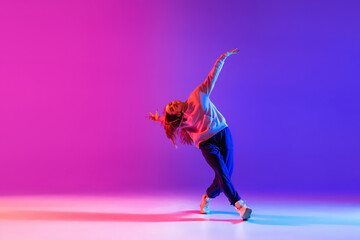 Young beautiful girl, female hip-hop dancer isolated on gradient pink purple neon studio background