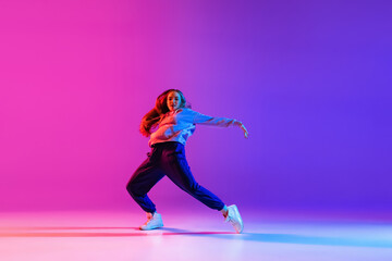 Young attractive girl, female hip-hop dancer isolated on gradient pink purple neon studio background