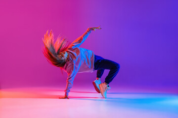 Attractive active young girl dancing and showing hip-hop tricks isolated on gradient pink purple neon studio background