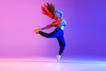 Young stylish girl dancing hip-hop isolated on gradient pink purple neon studio background