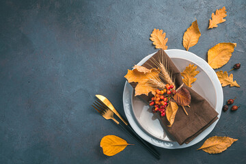 Thanksgiving Day background with cutlery, napkin and dry leaves on a dark gray-blue background. Top view, copy space.