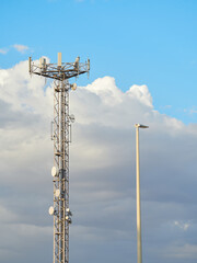 Vertical view against the evening sky of a telecommunication antenna tower with a defocused street lamp in the foreground