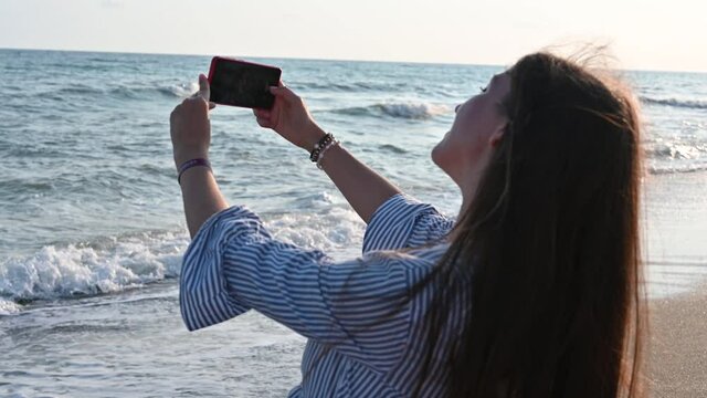 Young woman taking pictures of the sea as a keepsake 
