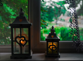 Stojące na parapecie okiennym w mieszkaniu lampiony z płonącymi wewnątrz nich świecami. © boguslavus