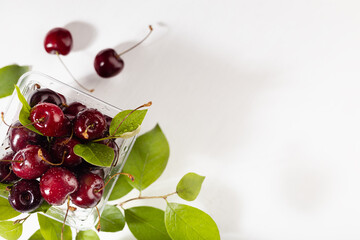 Summer takeaway food - wet ripe red fresh cherry in plastic box with green leaves on white wood board, copy space, top view, border.
