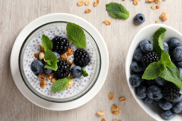 Delicious chia pudding with berries and granola on wooden table, flat lay