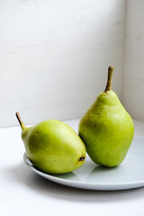 Two green pears in a gray plate on a white background. Minimalism. Culinary simpple preparation. Fresh and healthy fruits. Template for markets or restaurants. Empty space for your text or design.