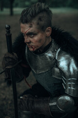 Portrait of medieval knight with bloody face in armour with sword.