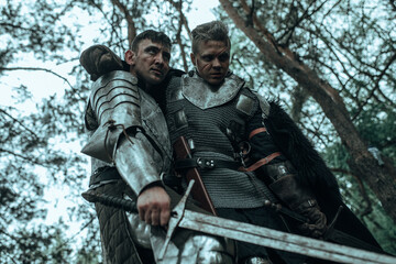 Medieval knight in armour supports and leads warrior wounded in battle.