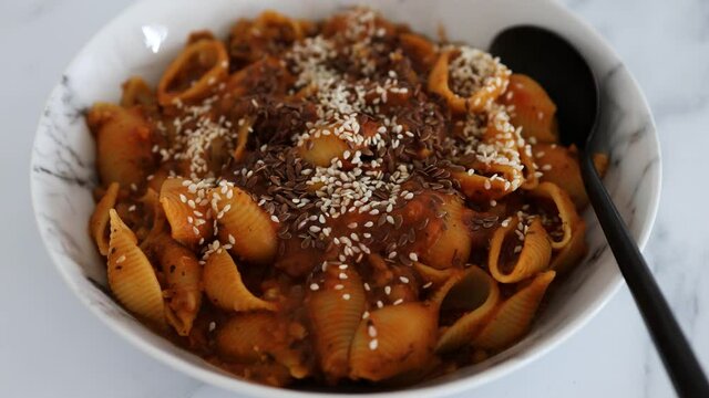 vegan shell pasta with lentil bolognese sauce topped with mixed seeds, healthy plant-based food