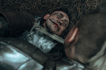 Medieval knight bends over lying enemy and puts a dagger to his throat.
