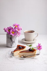 Slices of Homemade Basque burnt cheesecake on plate with blueberries and mint leaves, cup of black tea on light background with flowers in vase