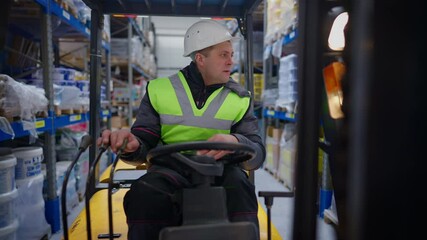 Warehouse loader driving forklift indoors looking around. Front view portrait of confident adult Caucasian man in hard hat and vest riding vehicle in storehouse. Live camera