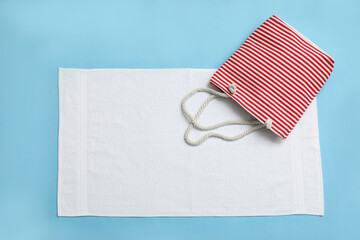 White towel and beach bag on light blue background, top view