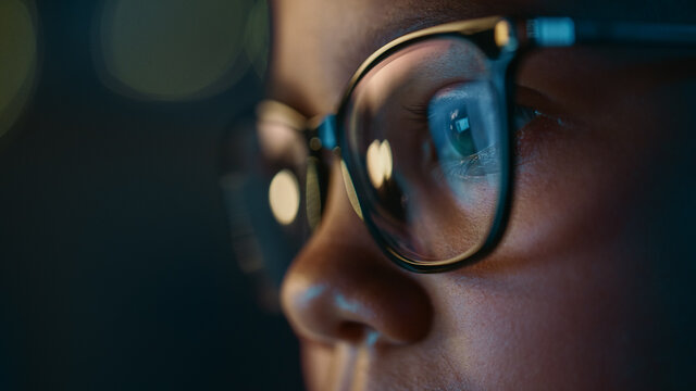 Close Up Portrait of a Cute Young Teenage Multiethnic Black Girl in a Dark Cozy Room at Home. Young Female Wears Glasses that Reflect School Homework from Her Laptop Computer Screen in Them.