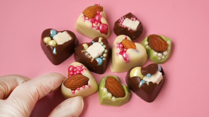 Pastry chef's hand in gloves holds a heart-shaped candy. Sweets on a pink background. Valentine's...