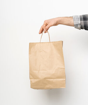 Man Hand In Plaid Shirt Twisted Sleeve Hand Holding Brown Paper Bag Isolated On White Background. Delivery Concept. Paper Bag For Takeaway Food. Delivery Carrying. 