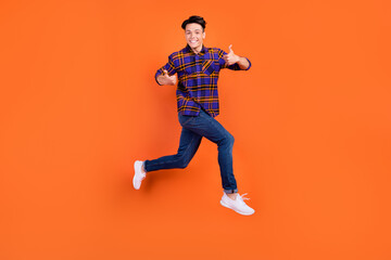 Fototapeta na wymiar Full size profile photo of young cool guy jump show thumb up wear shirt jeans sneakers isolated on orange background