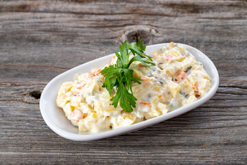 Traditional Russian salad with baked vegetables with mayonnaise in a bowl. Wooden background.