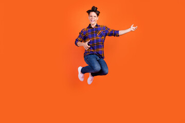Fototapeta na wymiar Photo of funky pretty teen boy wear plaid outfit spectacles smiling jumping high playing guitar isolated orange color background