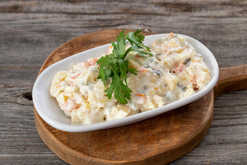 Traditional Russian salad with baked vegetables with mayonnaise in a bowl. Wooden background.