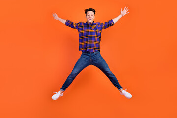 Fototapeta na wymiar Full length photo of young funky guy jump wear shirt jeans sneakers isolated on orange background