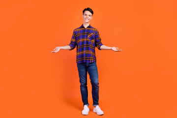 Photo of sweet cute teen boy wear plaid outfit spectacles smiling compare arms empty space isolated orange color background