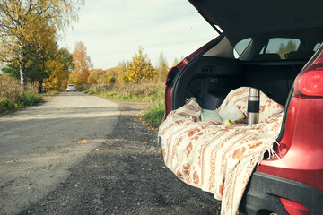 Road trip, local travel in fall season. Open car trunk with picnic gear and map near rural road....