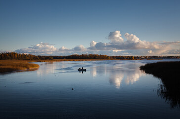 Seascape, calm sea with two fishermen on a boat and clouds reflecting on the blue water.