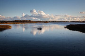 Seascape, calm sea with two fishermen on a boat and clouds reflecting on the blue water.