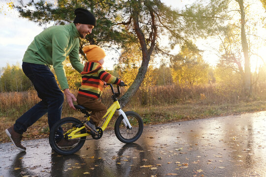 Father teaches his little child to ride bicycle in autumn park. Happy family moments. Time together dad and son. Candid lifestyle photo.