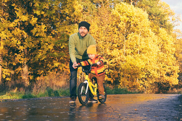 Father teaches his little kid to ride bike in autumn park. Child practicing cycling. Happy family...
