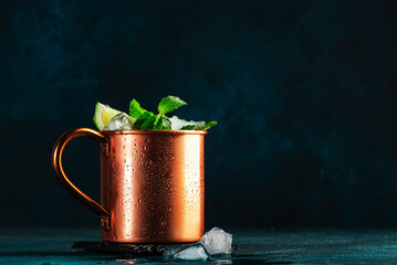 Moscow mule cocktail in copper mug with lime, ice, ginger beer, vodka and mint. Deep blue background
