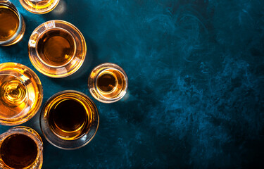 Strong alcohol drinks, hard liquors, spirits and distillates iset in glasses: cognac, scotch, whiskey and other. Blue background, top view - obrazy, fototapety, plakaty