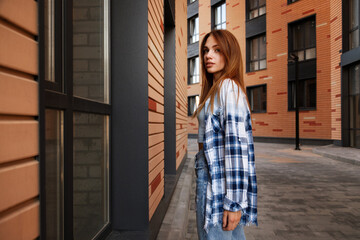 attractive brunette in a plaid shirt near a brown building urban style