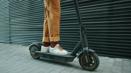 Low section shot of legs of unrecognizable man riding electric scooter on urban street