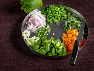 A Close up view of raw vegetables neatly cut in a steel plate against a dark background to prepare the delicious Indian 'Kichdi'  or Biryani dish.
