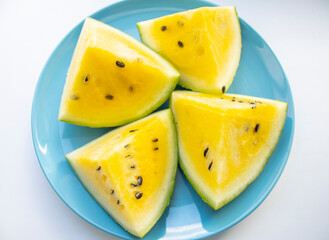 slices of watermelon with yellow pulp and seeds lie on a blue plate, on a light surface. Diet, fruits, seasonal vitamins. Yellow watermelon