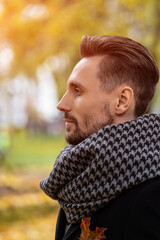 Face profile photo of handsome young man in dark blue coat and scarf or muffler. A young business man stands on the street in an autumn coat looks confidently sideways away.