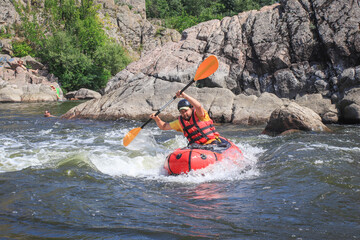 A man rowing inflatable packraft on whitewater of mountain river. Concept: summer extreme water sport,  active rest, extreme rafting.
