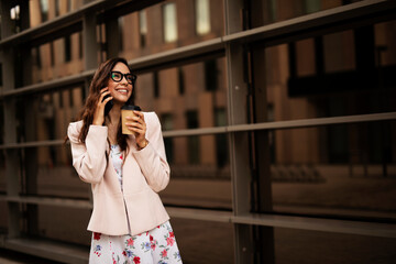 Young businesswoman talking to the phone. Female manager drinking coffee while walking through the city.