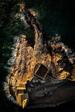 Top-down drone view of a rocky point with a small building jutting into the sea at golden hour, Cinque Terre, Italy