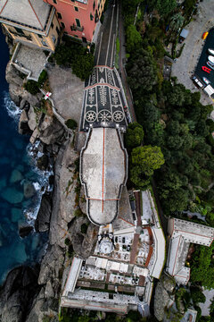 Top-down drone view of a clifftop church with a pebble mosaic forecourt and cemetery above the sea in Portofino, Italy
